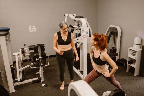 Free Two women doing exercise in a gym, featuring various gym equipment for a healthy lifestyle. Stock Photo