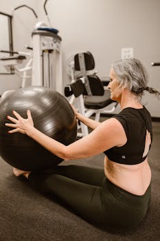 A midlife woman in activewear using a stability ball for fitness in an indoor gym.