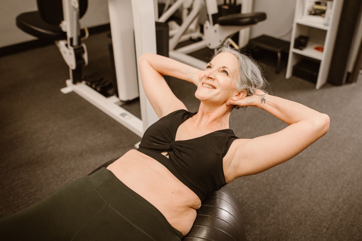 Una donna anziana sorridente si allena in palestra su una fitball