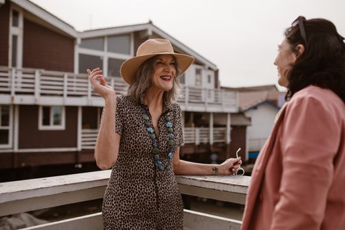 Free Two women enjoying a conversation on a wooden railing outside on a sunny day. Stock Photo