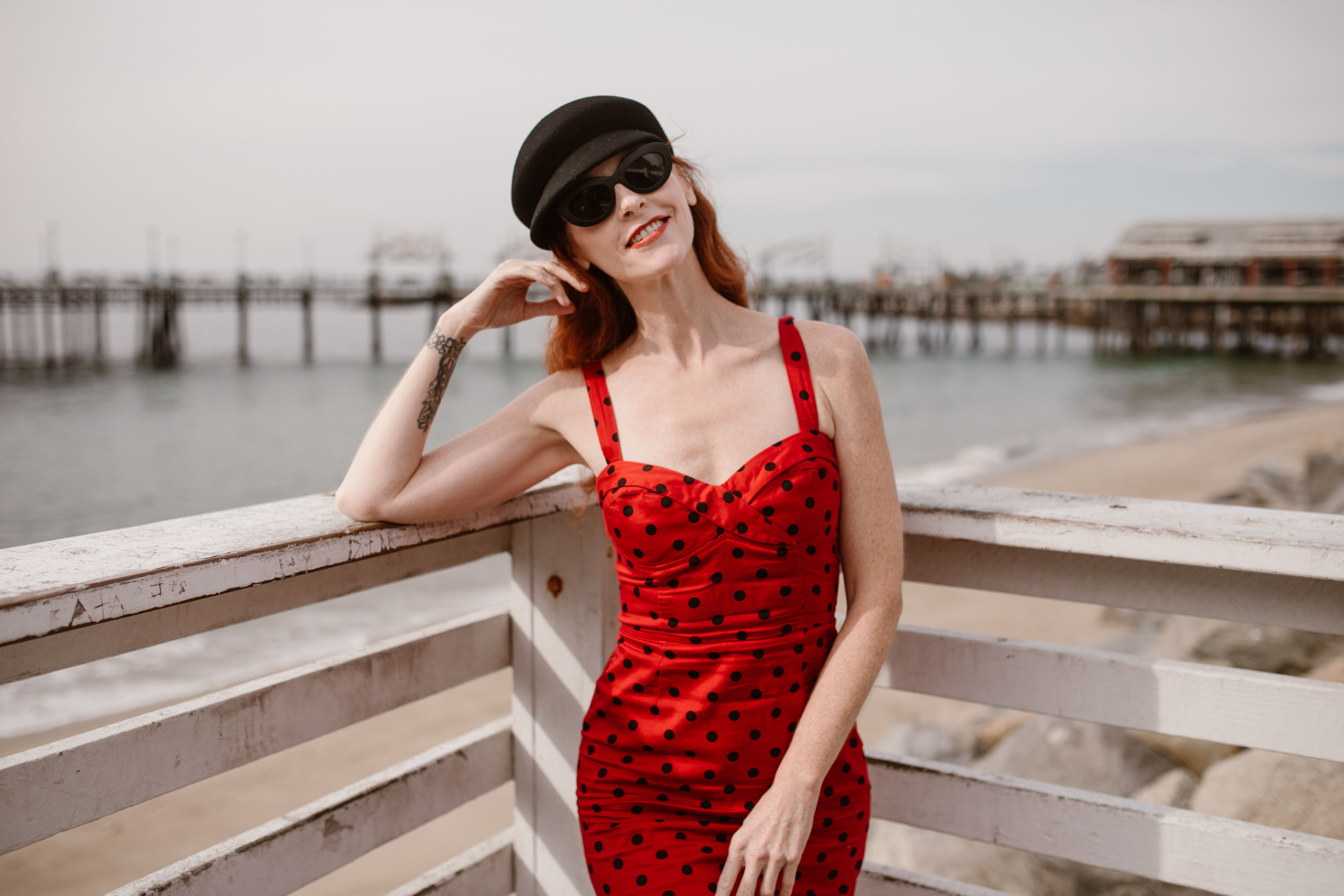 A Woman Wearing a Red Dress Leaning on a Wooden Railing · Free Stock Photo