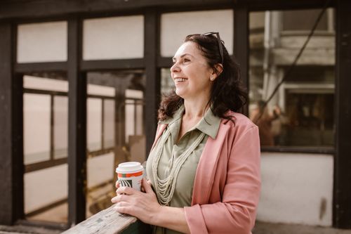 Free Mature woman happily holding coffee outdoors in an urban setting. Stock Photo