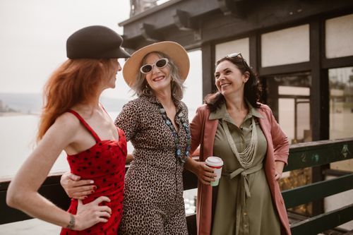 Free Three stylish women laughing and enjoying a sunny day outdoors. Friendship and joy. Stock Photo