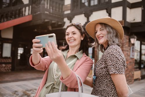 Free Two happy women taking a selfie outdoors in a stylish, summery setting. Stock Photo