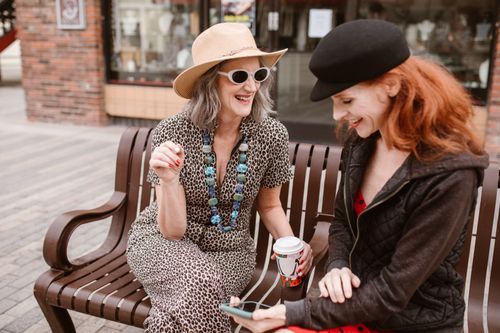 Free Two women laughing and enjoying coffee on a bench in an urban setting. Stock Photo
