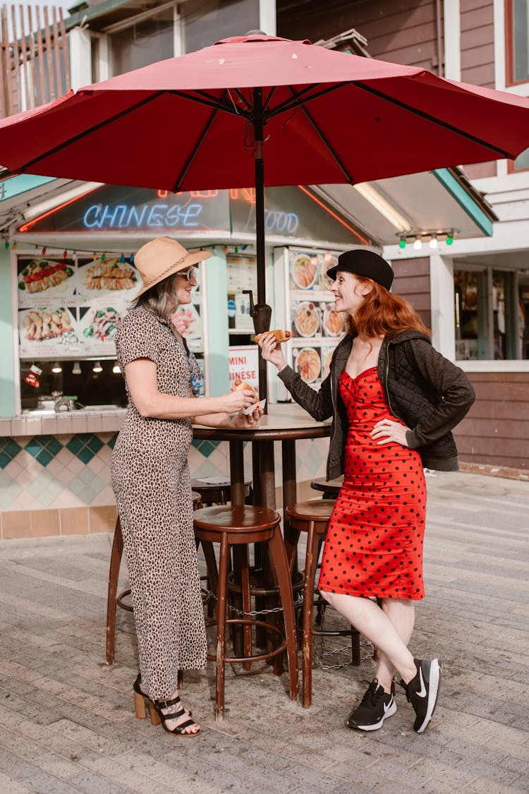 Two Women Talking While Holding Hotdogs