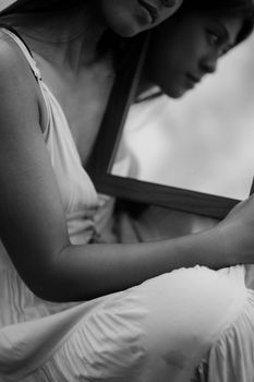 Artistic black and white photo of a woman holding a mirror, reflecting her image.