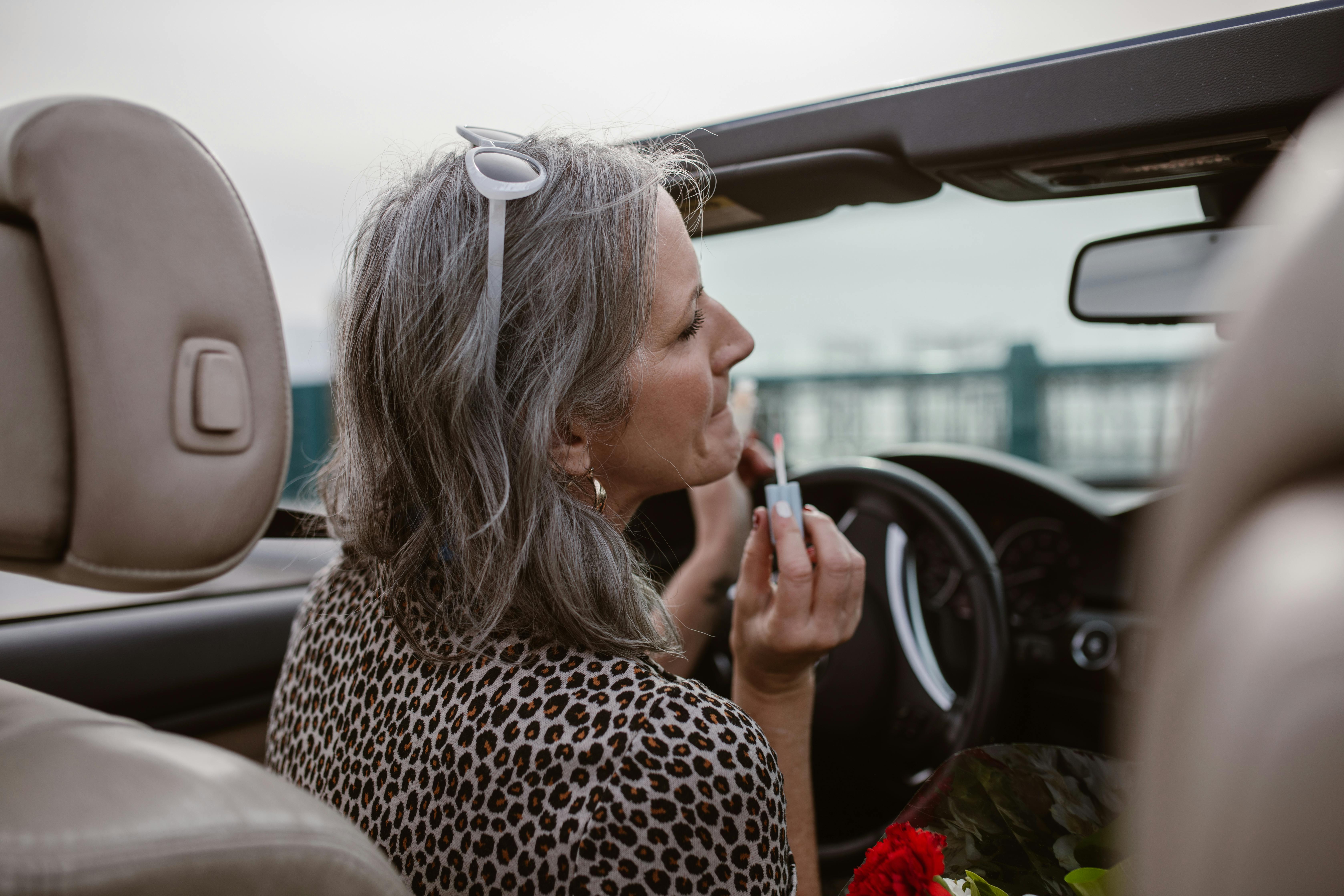 stylish woman applying lip gloss while driving car