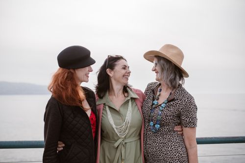Free Three women in stylish outfits smiling together outdoors by the sea. Stock Photo