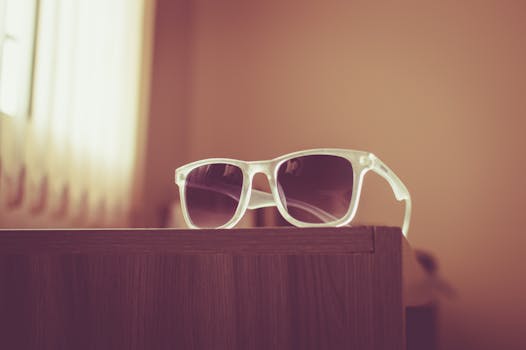 Close-up of modern sunglasses resting on a wooden table in a softly lit room.