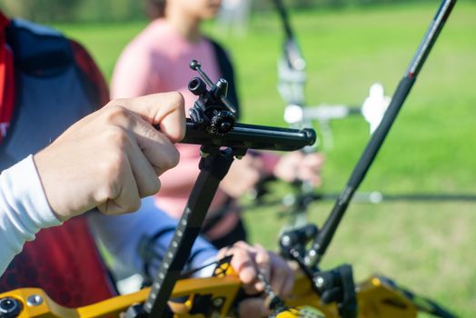 Detailed focus on adjusting an archery bow during a sports event outdoors.