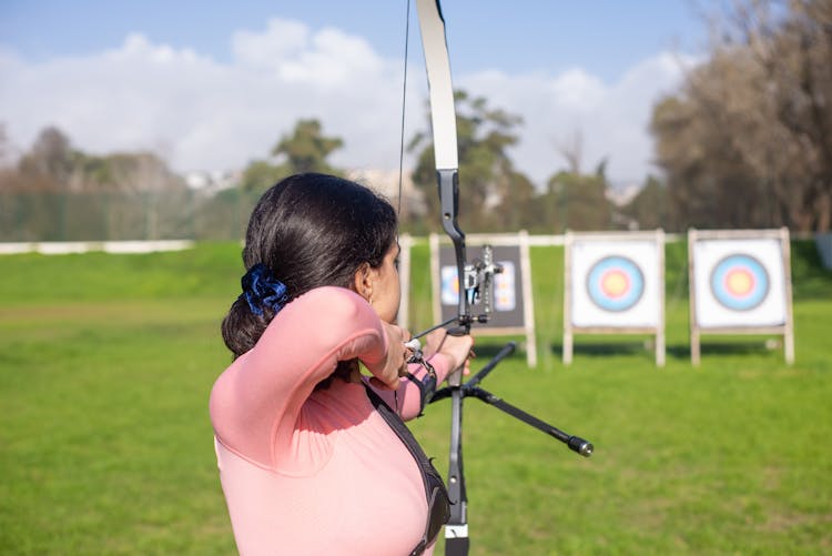 Woman Aiming Bow And Arrow On Archery Target Board