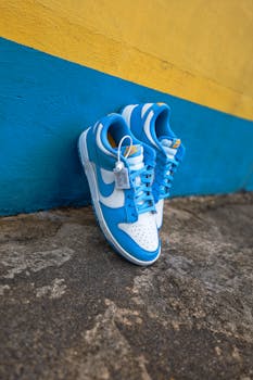 Pair of blue and white sneakers on textured ground with vibrant background.
