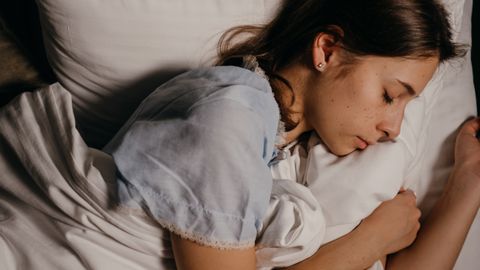 A serene young woman peacefully sleeping on a white pillow indoors at night.