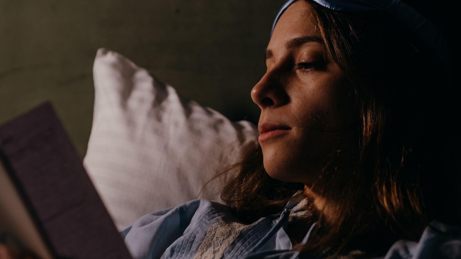 A woman reading in bed beside a blue sleep mask
