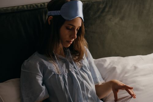 Free A woman in pajamas and sleep mask relaxing in bed, creating a cozy atmosphere. Stock Photo