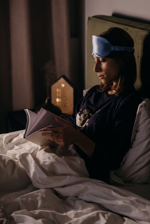 Free Woman Sitting on a Bed While Reading a Book  Stock Photo