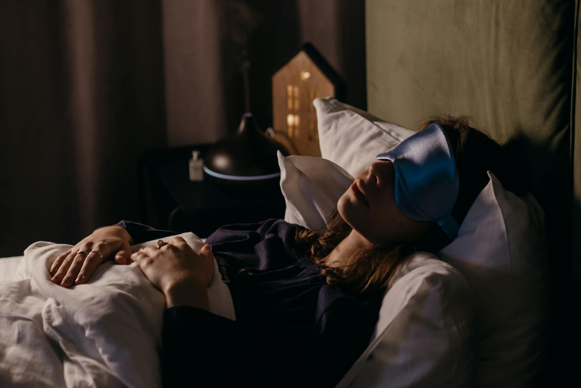 A woman resting with a sleep mask in a calm bedroom setting, creating a serene and cozy atmosphere.