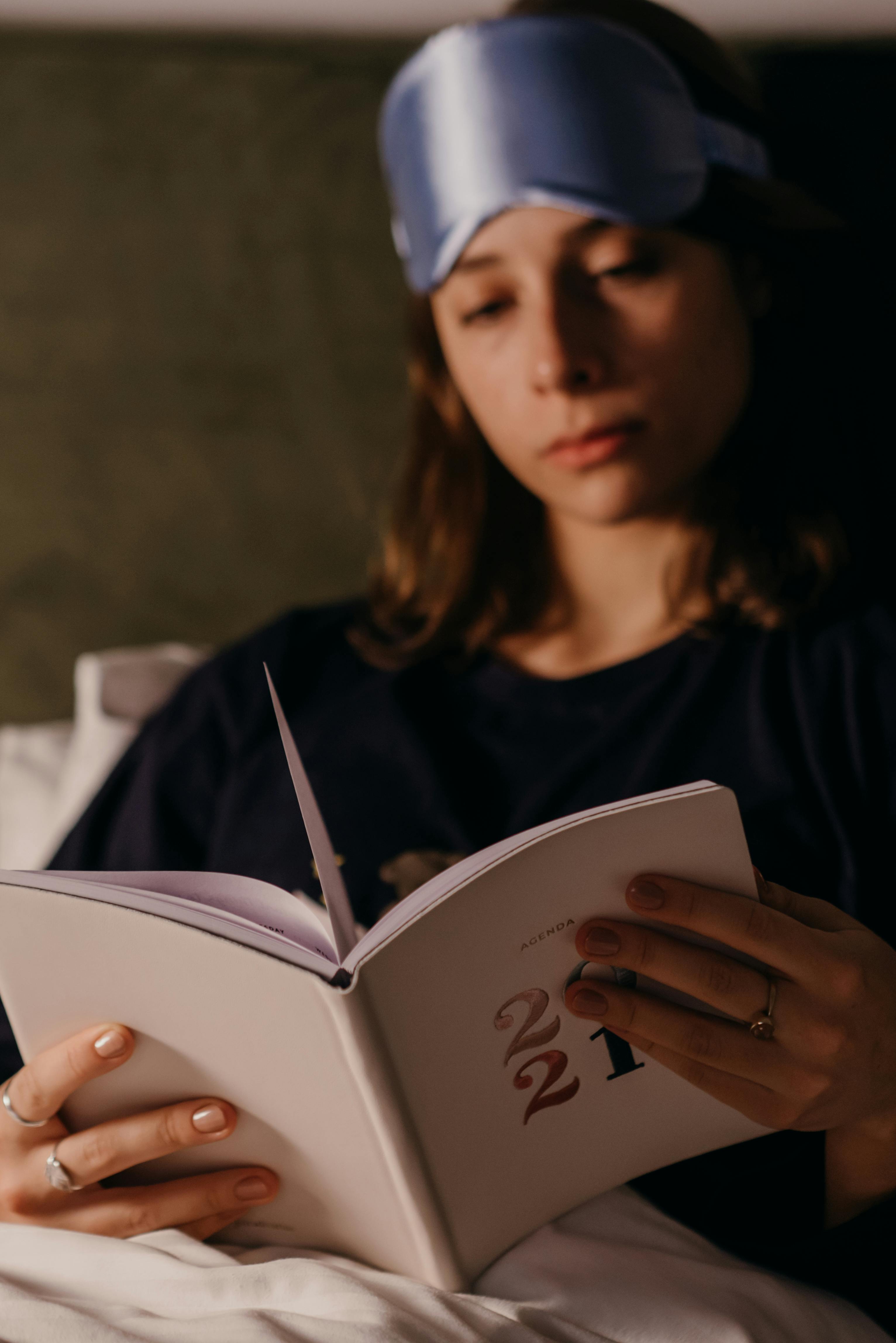 Woman reading a book in bed with a sleep mask, capturing a cozy nighttime vibe.