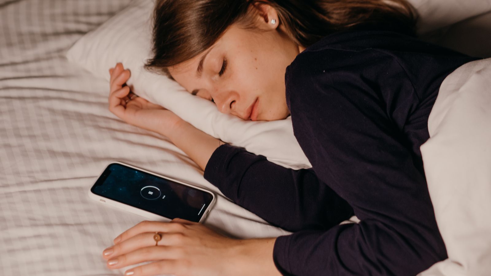 A woman peacefully sleeping in bed with a smartphone nearby, conveying rest and relaxation.