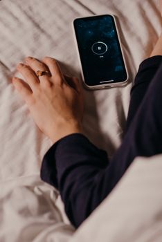 A person relaxing in bed with a smartphone playing music, perfect for leisure or technology themes.