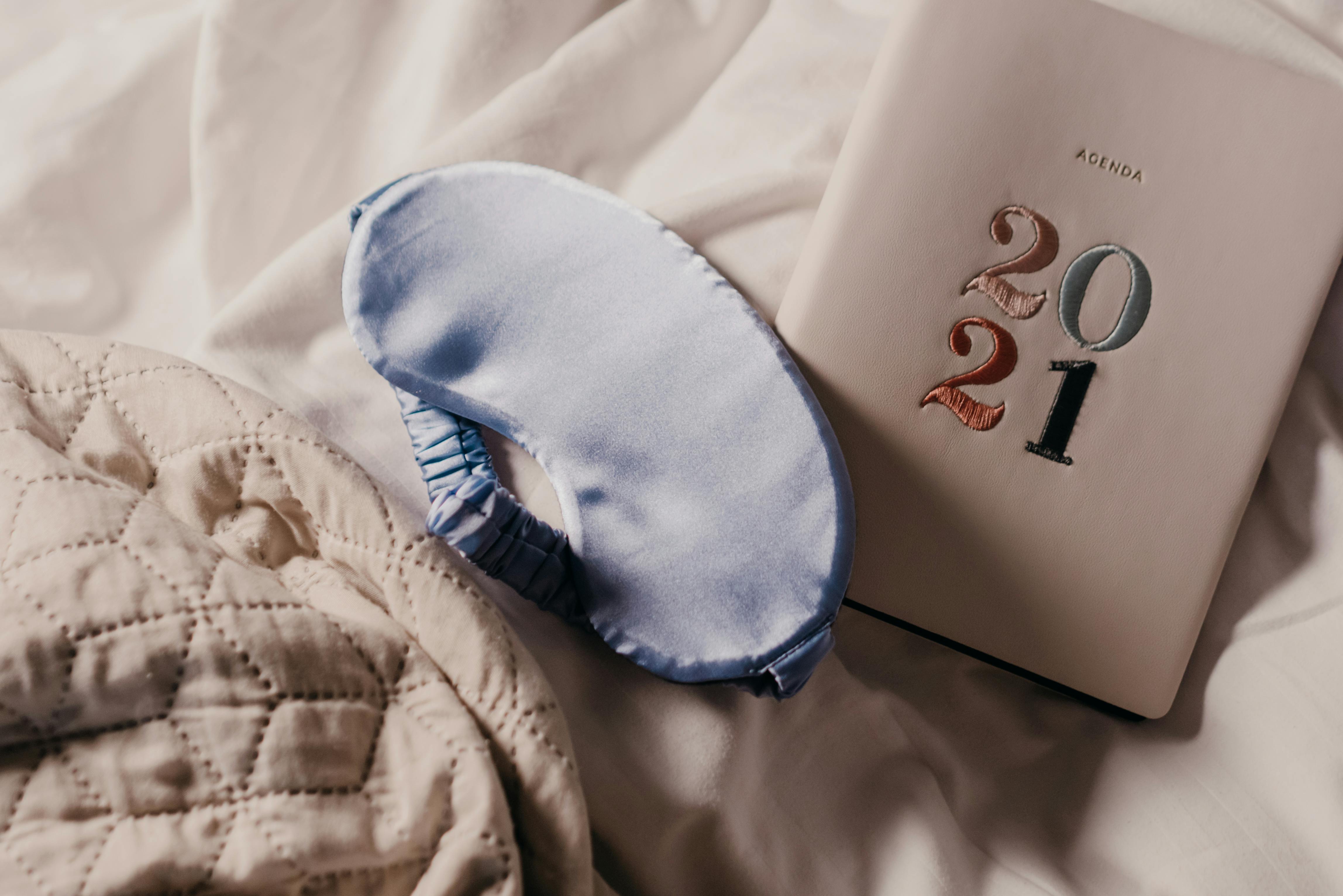 A soft blue sleep mask and 2021 planner on a quilted bedspread create a serene setting.