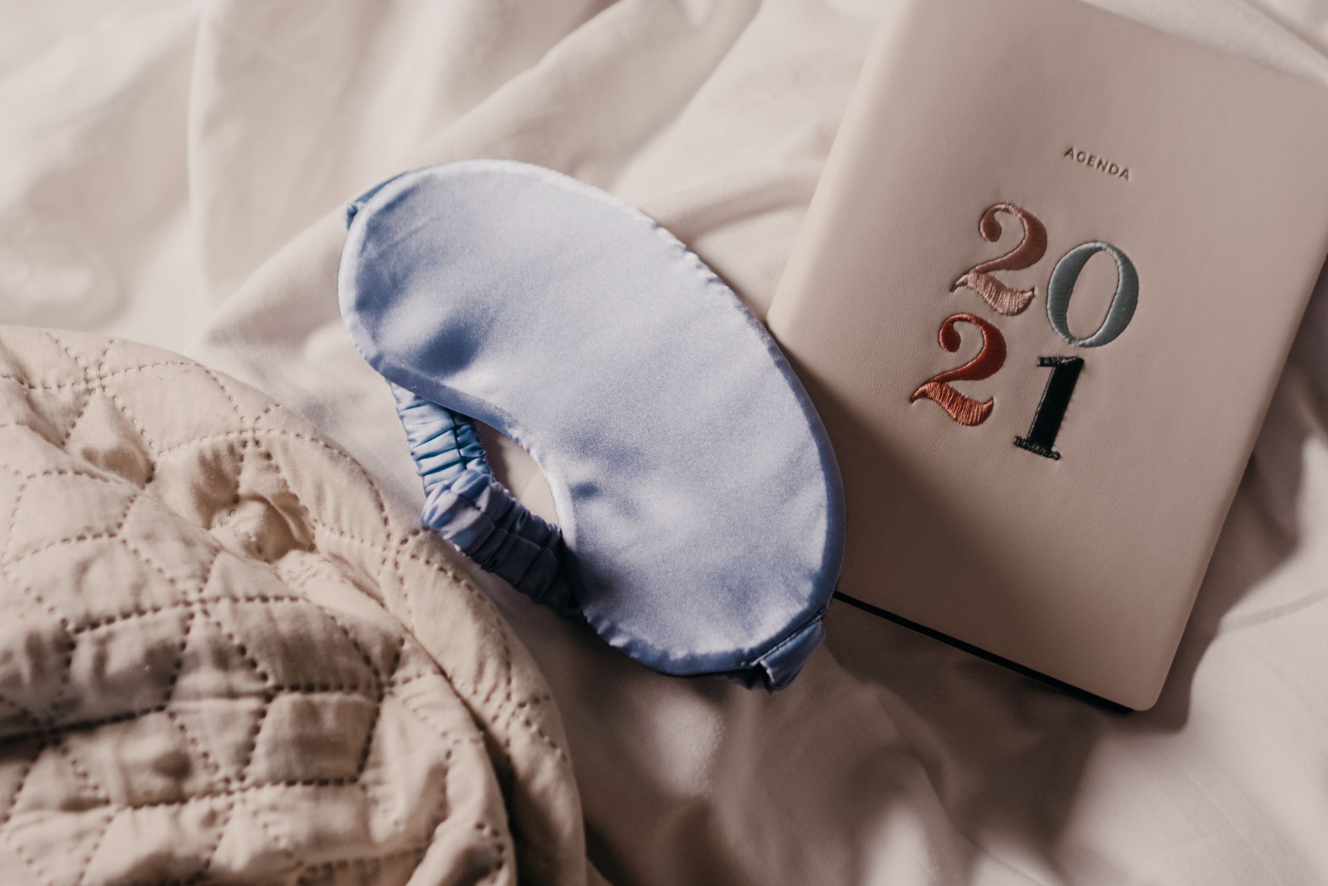 A soft blue sleep mask and 2021 planner on a quilted bedspread create a serene setting.