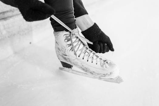 Close-up shot of a person tying ice skates on a rink, captured in black and white.