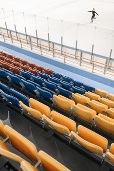 Empty ice rink with colorful seats and lone figure skater in motion.