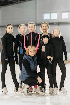 A group of young figure skaters posing with their coach at an indoor ice rink.