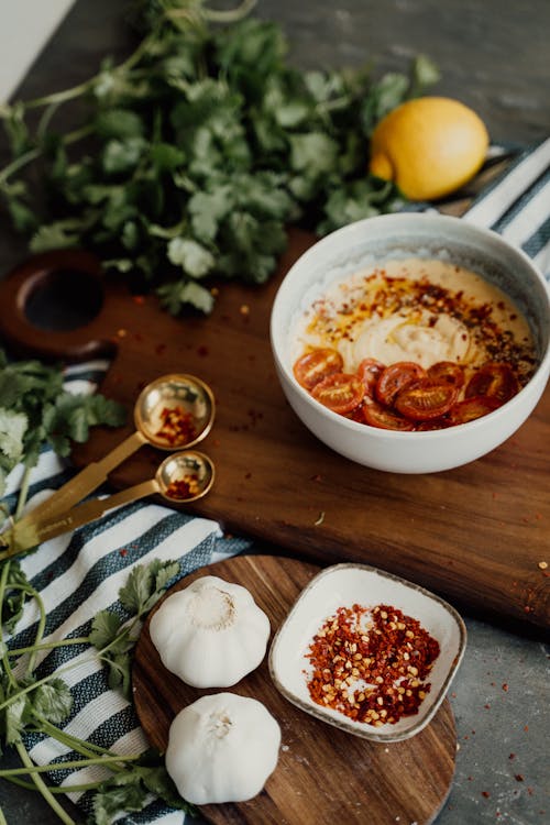 Free Bowl with Hummus and Tomatoes Standing on a Cutting Board with Herbs  Stock Photo