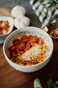 Delicious bowl of creamy hummus topped with cherry tomatoes and spices on a rustic wooden table.