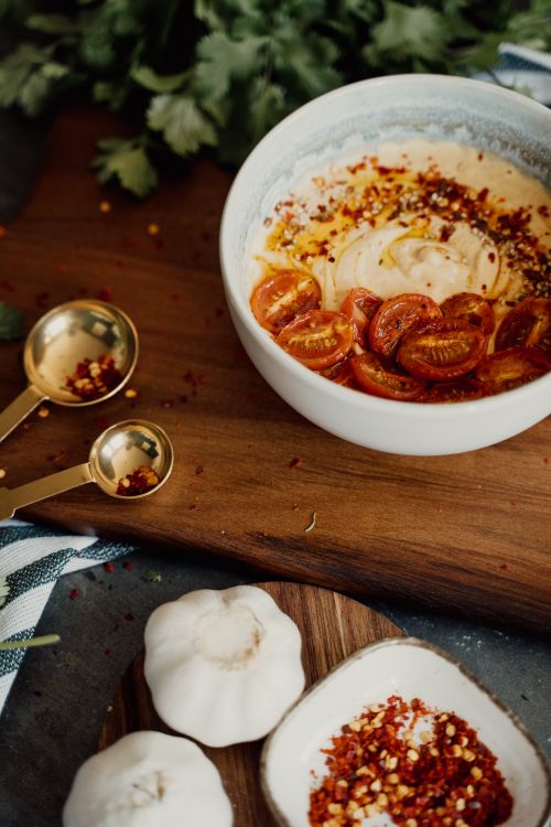 Free Delicious hummus topped with cherry tomatoes and spices, served on a rustic wooden board. Stock Photo