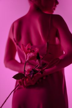 Artistic portrait of a person holding a lily under vibrant neon pink lighting.
