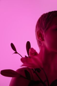 Creative side portrait of a woman with flowers against a pink background, showcasing unique lighting.