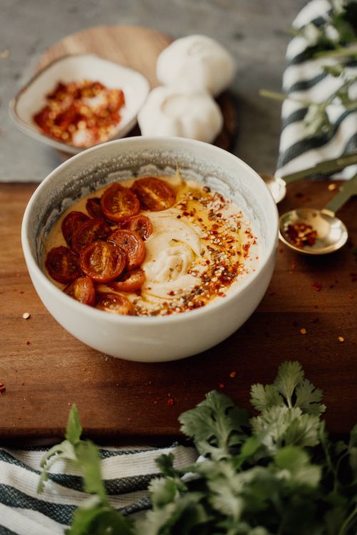 Free A savory vegan hummus bowl topped with cherry tomatoes and chili flakes, perfect for a healthy snack. Stock Photo