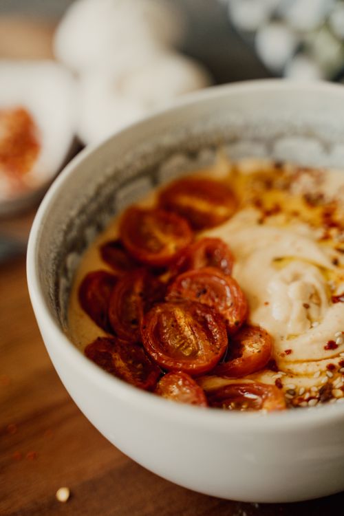 Free Delicious hummus bowl topped with roasted cherry tomatoes and spices, perfect for a healthy meal. Stock Photo