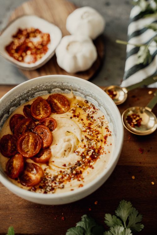 Free Close-up of a bowl of hummus topped with cherry tomatoes and spices, creating a healthy and tasty dish. Stock Photo
