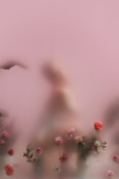 Blurred silhouette among translucent flowers on a soft pink background, creating an artistic dreamy effect.
