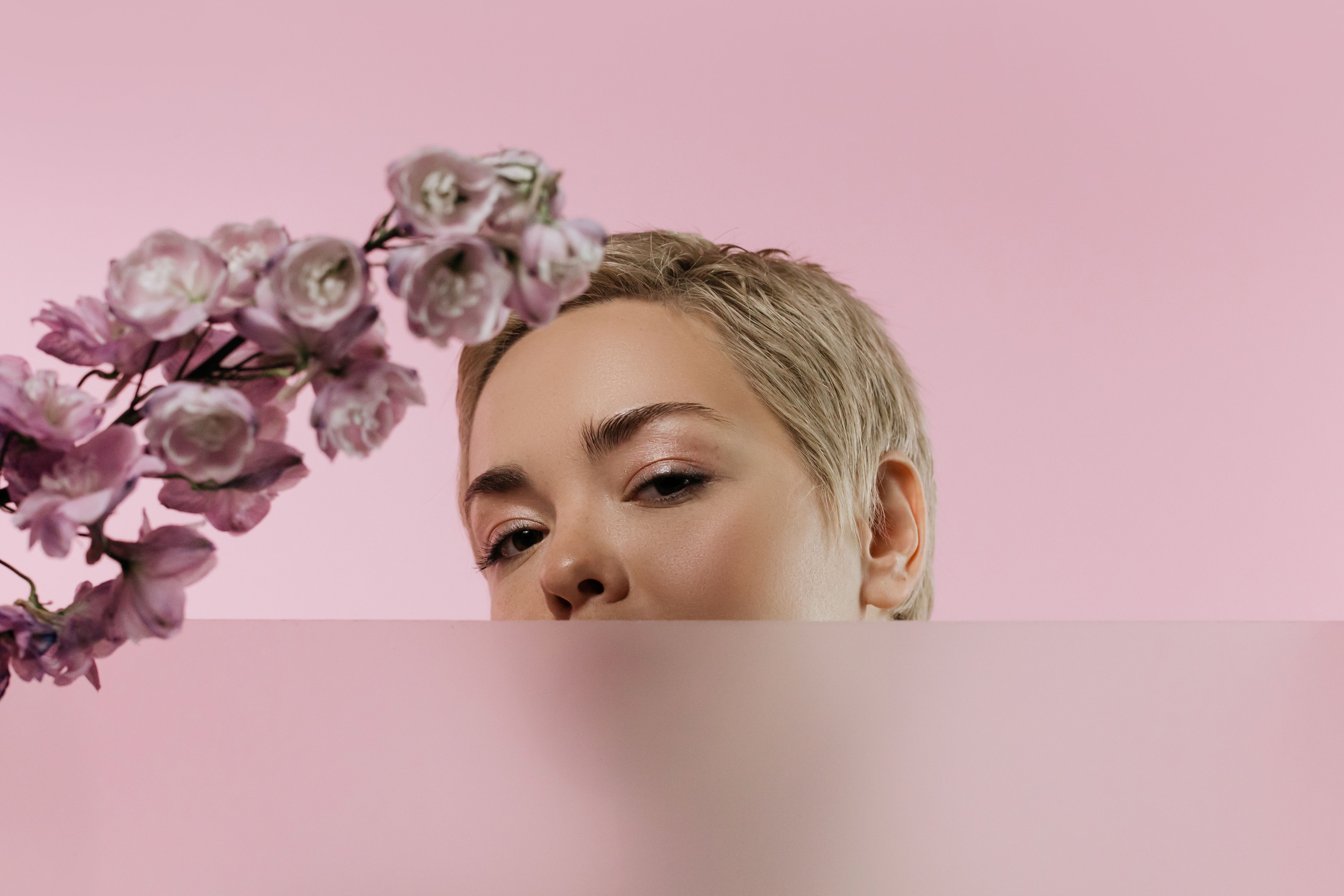Artistic portrait of a woman with short blonde hair, pink flowers, and a pink background.