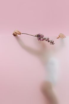 Blurred artistic silhouette of a woman with flowers on a pink background, creating a dreamy and ethereal feel.
