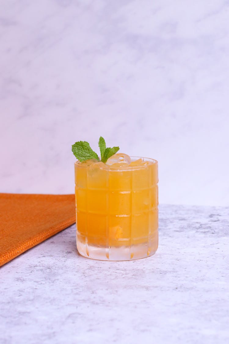 Glass Of Orange Lemonade With Ice On Light Background