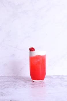 Vibrant raspberry cocktail with foam on marble surface.