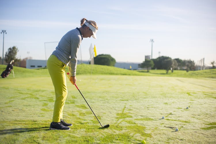 A Side View Of A Woman Standing On Green Grass While Playing Golf