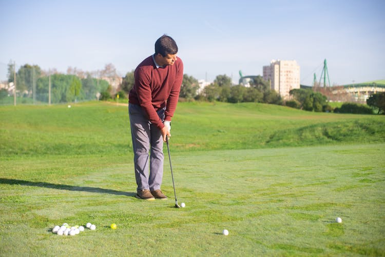 A Man In Red Sweater Standing On The Field While Playing Golf