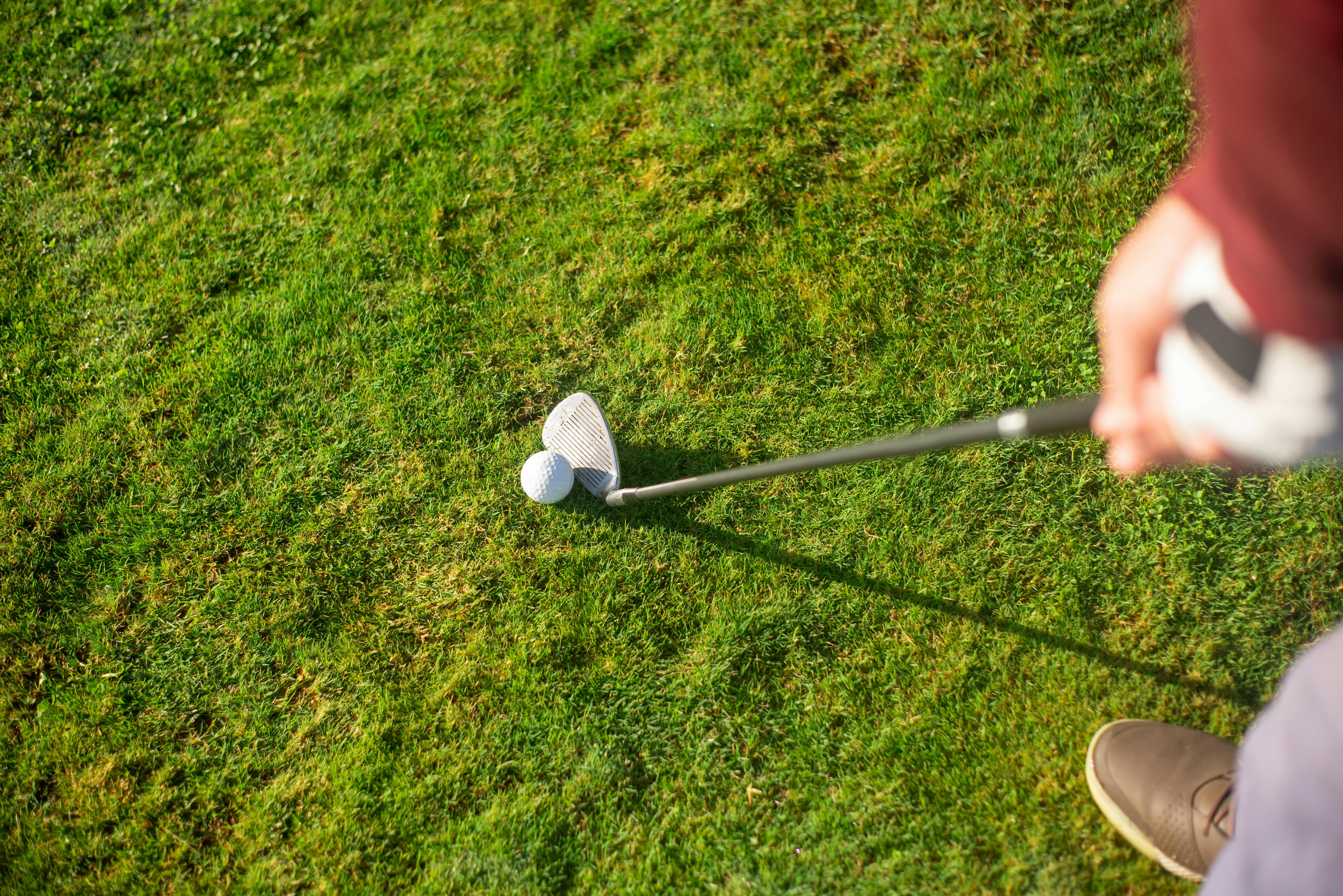 a person holding a golf club near the ball on green grass