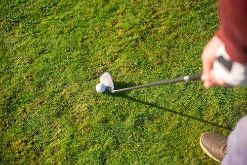 Free A Person Holding a Golf Club Near the Ball on Green Grass Stock Photo