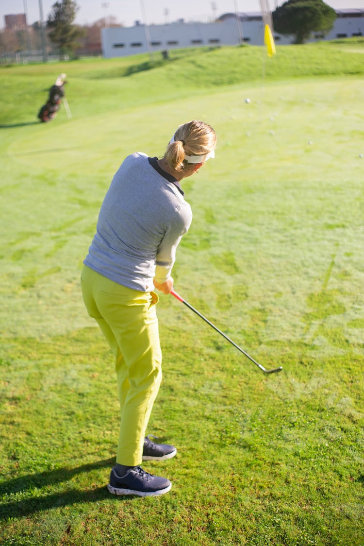 A Woman In Yellow Pants Standing On The Field While Playing Golf