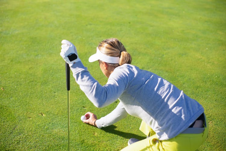 A Woman In Gray Sweater Putting A Golf Ball On Green Grass