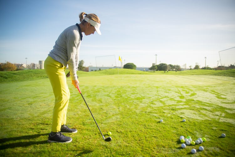 A Side View Of A Woman Standing On Green Grass While Playing Golf